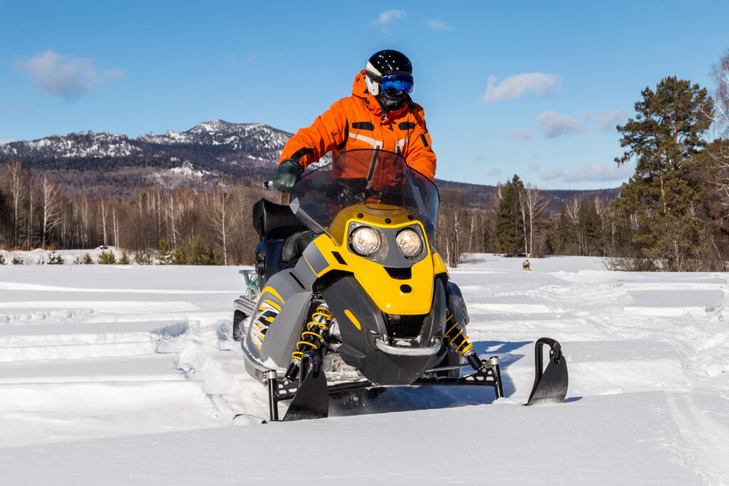 A snowmobile rider in orange on a yellow snowmobile in deep snow