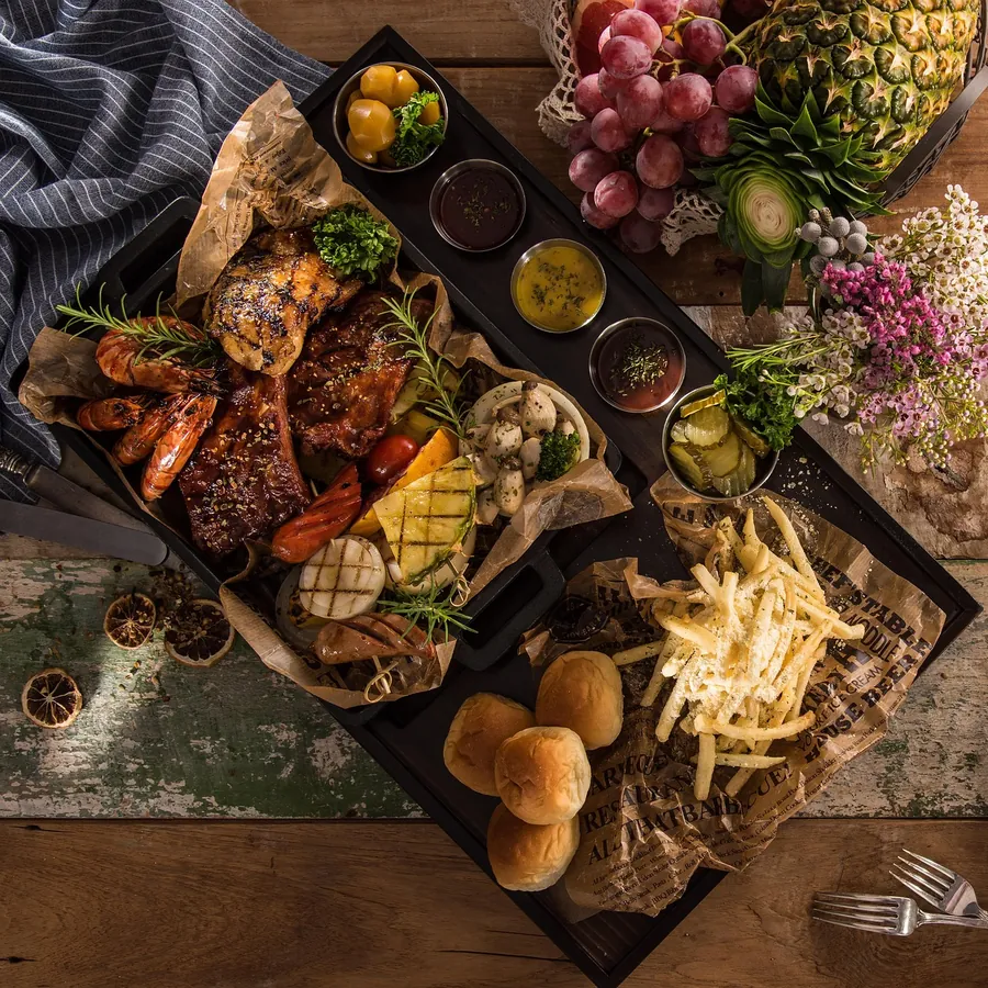 A festive feast board with grilled meat, prawns, sauces, bread rolls and fries